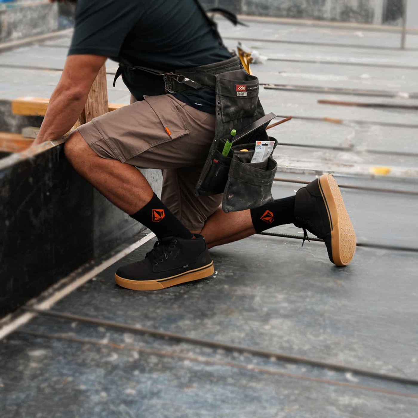 Black skate work shoes with gum outsole on a worker kneeling at a construction site