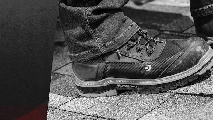 Close-up of black safety work boots on a shingle roof, worn with jeans, featuring carbon fiber texture and rugged outsole